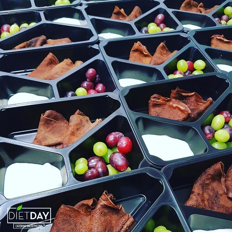 Dietetyczne pudełka cateringowe z naleśnikami czekoladowymi, białym kremem i mieszanką zielonych i czerwonych winogron, ułożone w rzędach z logo 'Diet Day' w lewym dolnym rogu.