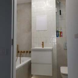 REDOMO.PL - Piotr Oleksiak - Usługi remontowo-budowlane - Nowoczesna łazienka po remoncie: białe płytki, złota armatura, podświetlana wanna i minimalistyczna szafka pod umywalką. Widoczne silikony budowlane.