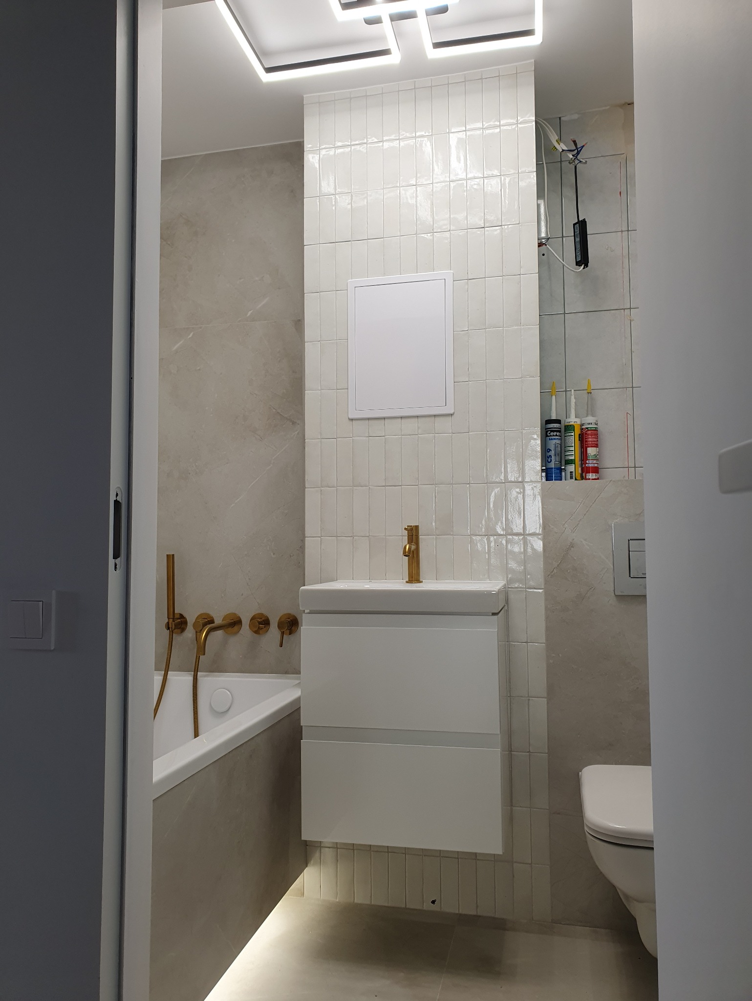 Nowoczesna łazienka po remoncie: białe płytki, złota armatura, podświetlana wanna i minimalistyczna szafka pod umywalką. Widoczne silikony budowlane.
