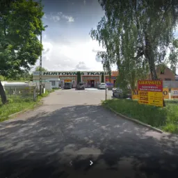 Fasada Hurtowni Tkanin Gaurangtex z Rzgowa, widok z ulicy, szyldy reklamowe po bokach, zaparkowane samochody na placu przed budynkiem.