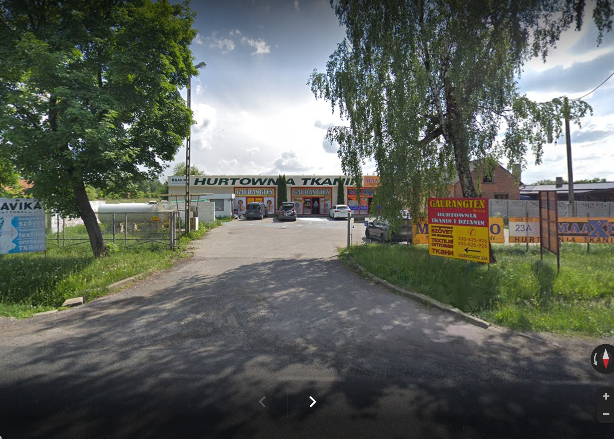 Fasada Hurtowni Tkanin Gaurangtex z Rzgowa, widok z ulicy, szyldy reklamowe po bokach, zaparkowane samochody na placu przed budynkiem.