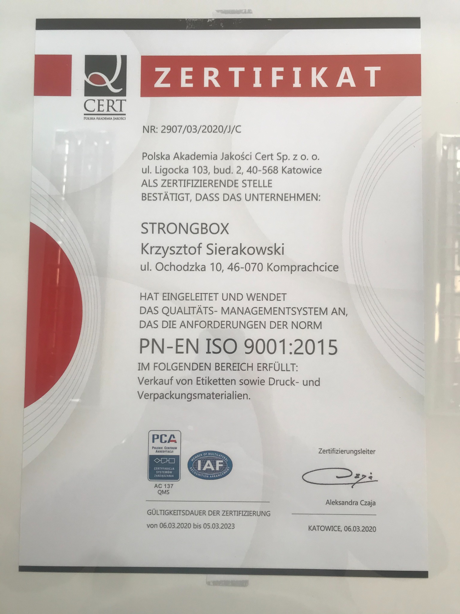 Certyfikat jakości ISO 9001:2015 dla firmy Strongbox, potwierdzający sprzedaż etykiet, materiałów do druku i pakowania, wydany przez Polską Akademię Jakości w Katowicach, z datą ważności do 05.03.