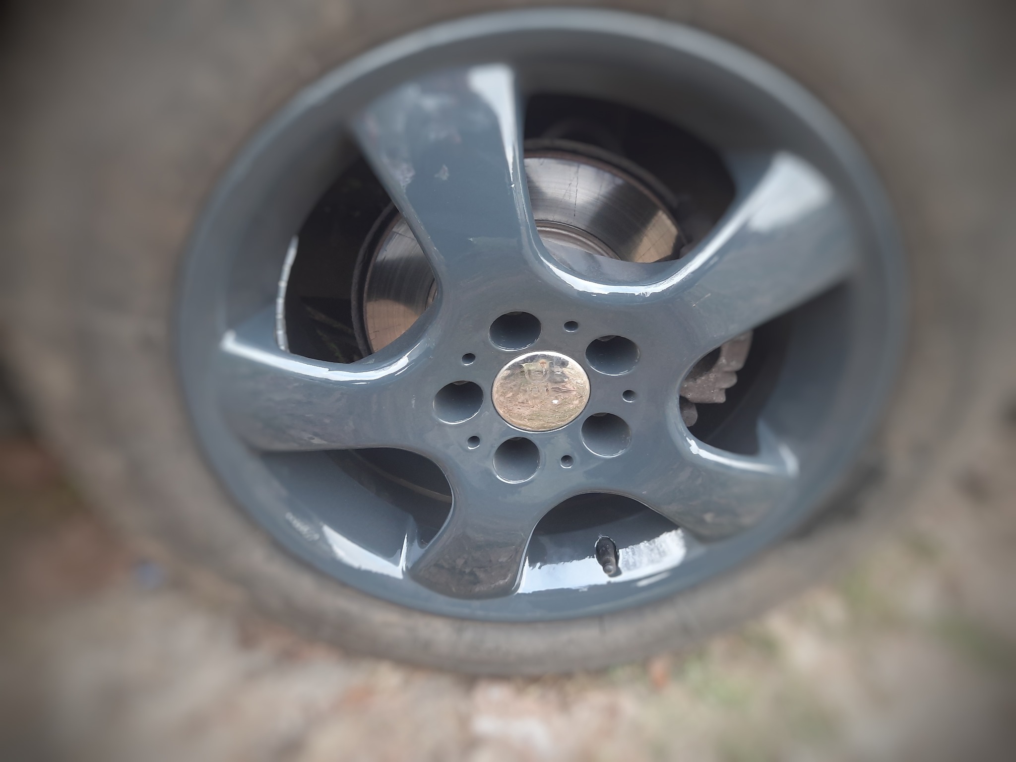 Szara felga aluminiowa z widoczną tarczą hamulcową, po renowacji z połyskiem, z delikatnymi niedoskonałościami lakieru na krawędziach.