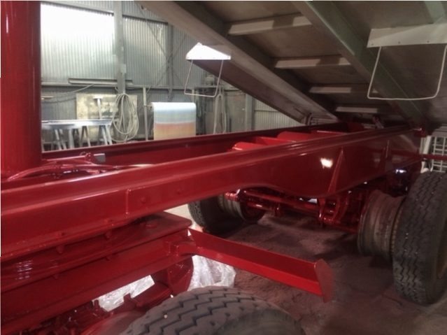 Czerwona rama naczepy po renowacji, widoczne świeżo pomalowane elementy podwozia i koła w warsztacie.