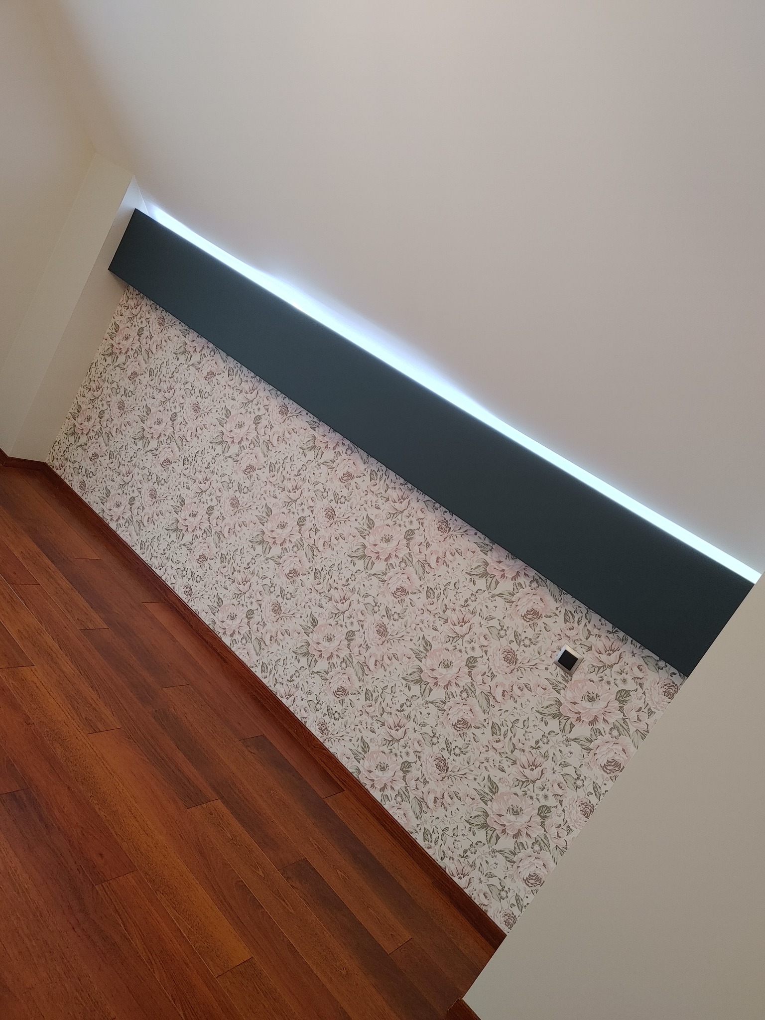 Pokój na poddaszu z drewnianą podłogą, ścianą w kwiaty i podwieszonym sufitem z oświetleniem LED.