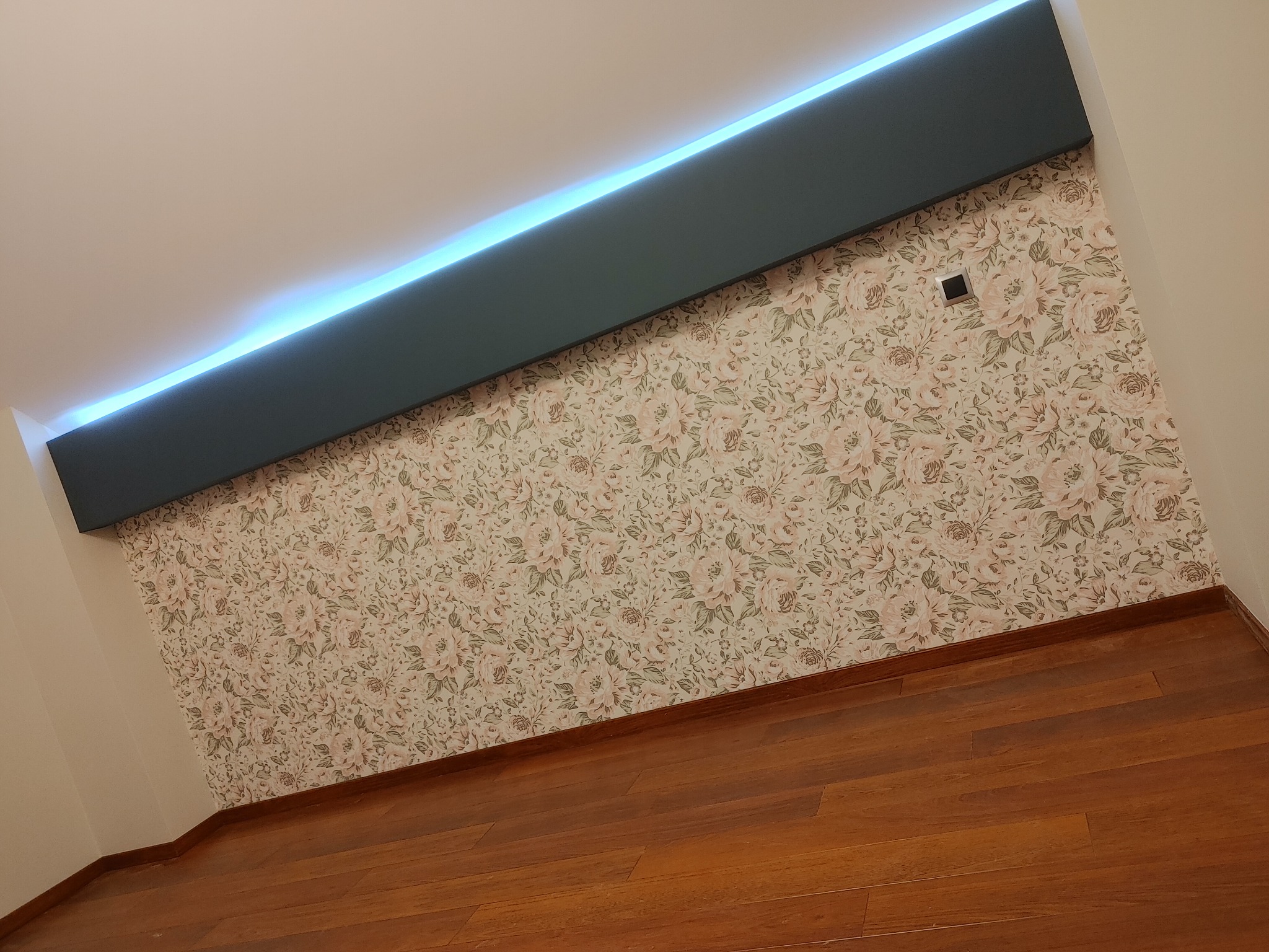 Wnętrze pokoju w Krakowie po remoncie: drewniana podłoga, ściana w kwiaty i podwieszany sufit z oświetleniem LED.