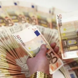 Stos 50-euro banknot&oacute;w trzymanych w dłoniach, z rozłożonym wachlarzem banknot&oacute;w w tle.