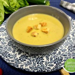 Catering Dietetyczny Blue - Kremowa zupa z grzankami w szarej misce na dekoracyjnym talerzu, serwowana przez firmę z Warszawy, z dodatkiem świeżych warzyw i lnianej ściereczki w kratę.