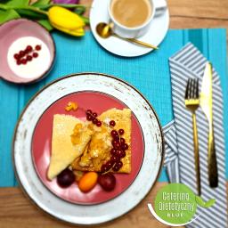 Catering Dietetyczny Blue - Elegancko podane naleśniki na różowym talerzu z owocami, orzechami i sosem, obok filiżanka kawy, sztućce w złotym kolorze i kwiaty na turkusowej podkładce. Widoczne logo firmy cateringowej BLUE.