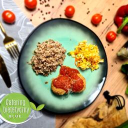 Catering Dietetyczny Blue - Kompozycja dania na turkusowym talerzu: kasza gryczana, surówka z kapusty i kotlety w sosie pomidorowym, uzupełniona o pomidorki koktajlowe, paprykę, bakłażana i złote sztućce na drewnianym tle.