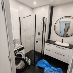 VINSTA SPÓŁKA CYWILNA WOJCIECH PAJĄK, DMYTRO ZHULINSKYI - Nowoczesna łazienka z czarno-białymi płytkami imitującymi marmur, kabiną prysznicową typu walk-in z czarnymi profilami, okrągłym lustrem z czarną ramą, białą szafką pod umywalką z czarnymi...