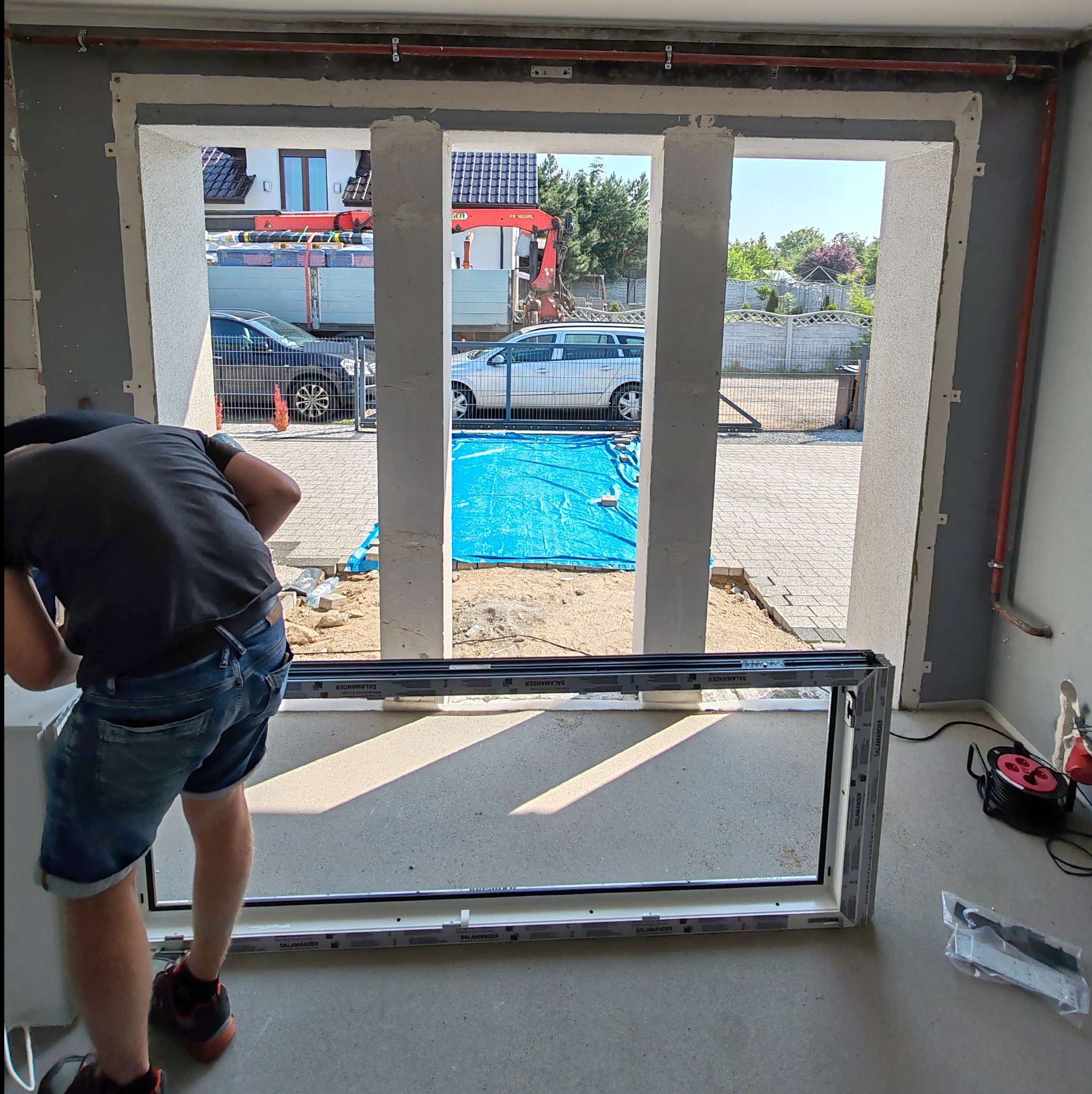 Montaż okna PCV Salamander w surowym otworze okiennym, widoczny dźwig budowlany za oknem.