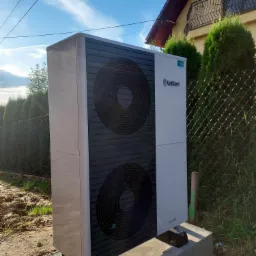 Nowa pompa ciepła Vaillant aroTHERM zamontowana na betonowym fundamencie przed domem jednorodzinnym, widoczne dwa wentylatory i logo producenta.