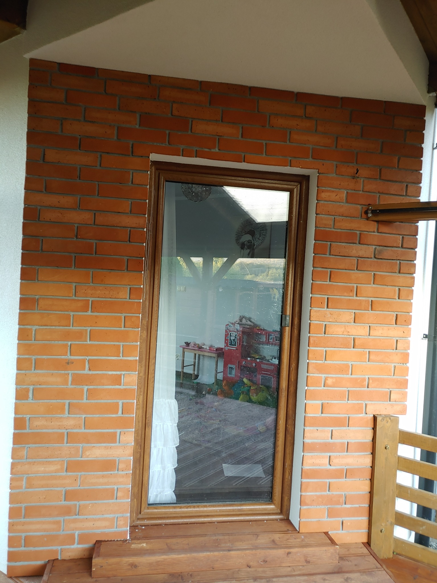 Elewacja z cegły klinkierowej wokół drzwi balkonowych z widocznym wnętrzem pokoju dziecięcego i drewnianym progiem.