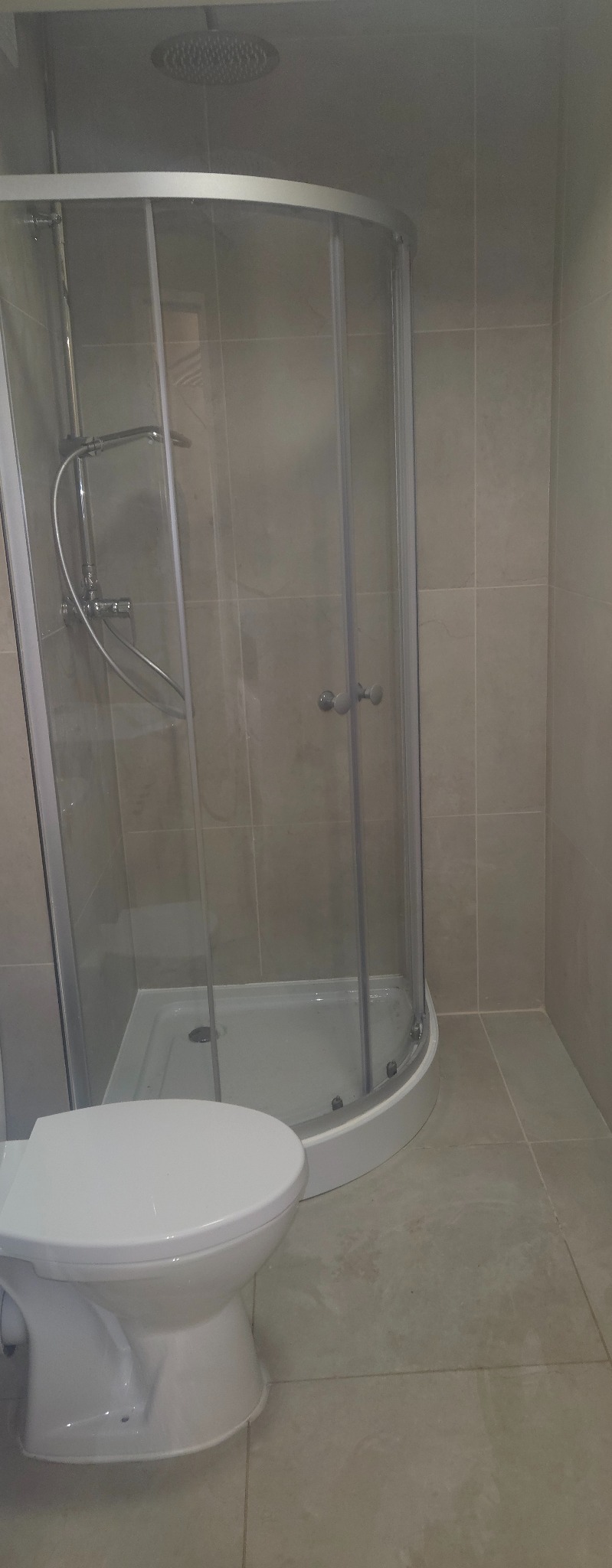 Nowoczesna łazienka z kabiną prysznicową typu walk-in i podwieszaną toaletą. Jasne płytki na ścianach i podłodze. Minimalistyczny design.