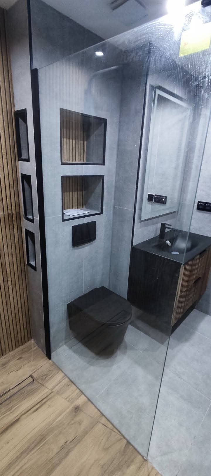 Nowoczesna łazienka z szarą armaturą, drewnianymi akcentami i szklaną kabiną. Minimalistyczny design z wbudowanymi półkami i podwieszaną toaletą.