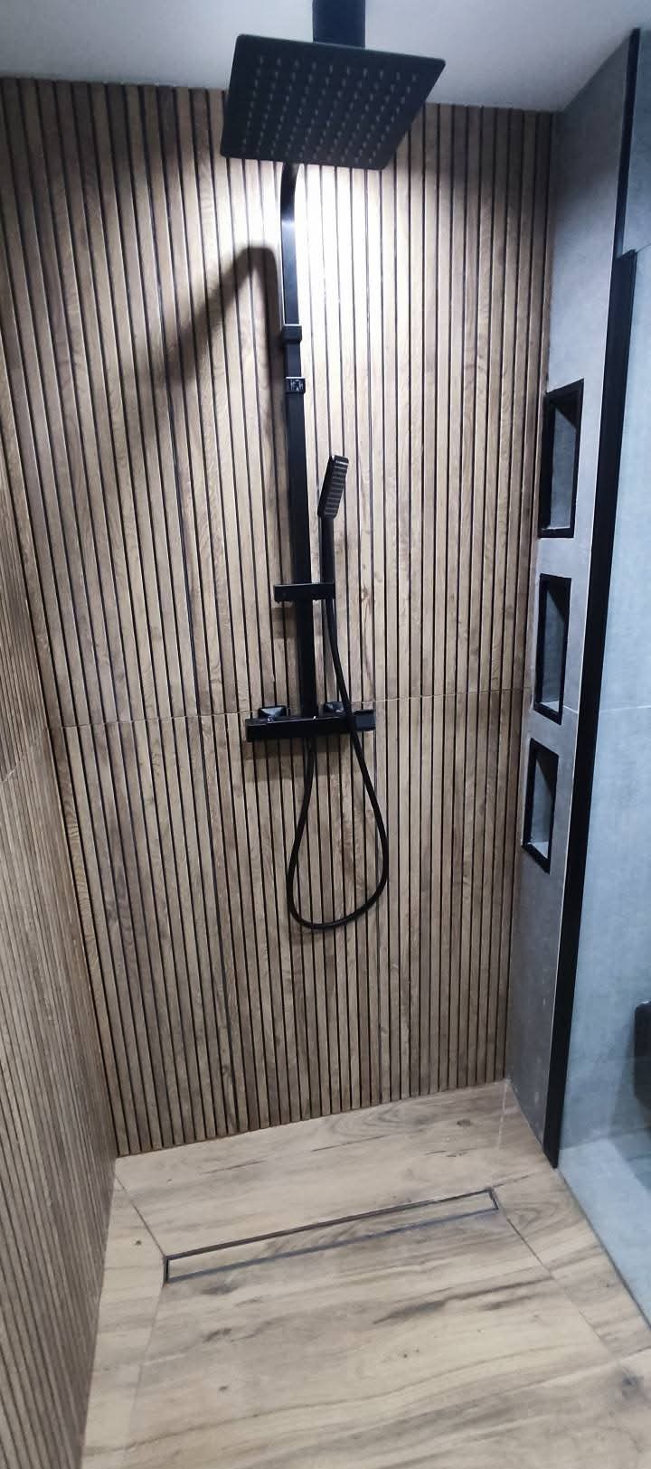 Nowoczesna kabina prysznicowa z drewnianą okładziną ścienną i czarną armaturą. Minimalistyczny design z wnękami w ścianie. Ukończony projekt łazienki.