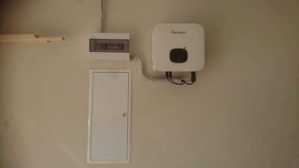 Biały inwerter Growatt zamontowany na ścianie obok skrzynki elektrycznej i małych drzwiczek rewizyjnych.