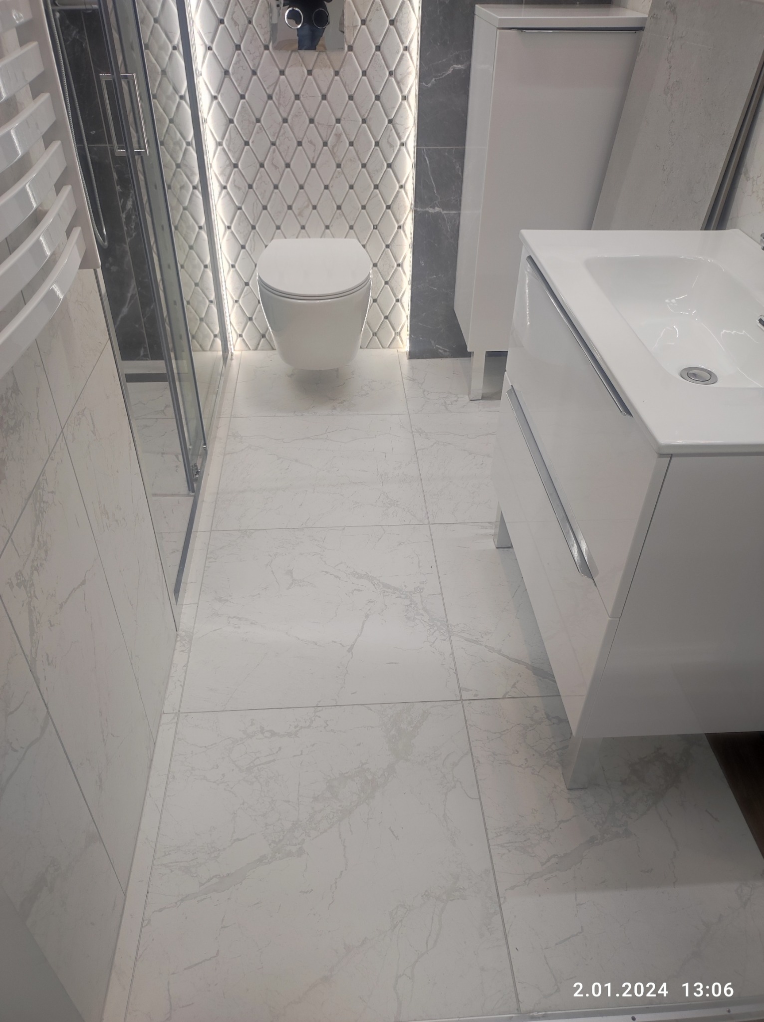 Nowoczesna łazienka z białą ceramiką, umywalką z szafką i kabiną prysznicową, wykończona jasnymi płytkami imitującymi marmur oraz dekoracyjną mozaiką diamentową z podświetleniem LED.