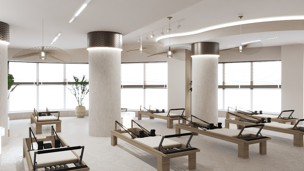 Jasne, przestronne studio pilates z beżowymi ścianami, dużymi oknami i rzędami drewnianych reformerów. Dekoracyjne lampy wiszą z sufitu.