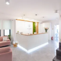 Jasne wnętrze kliniki z recepcją, różową sofą i schodami z dekoracyjnymi świecami.