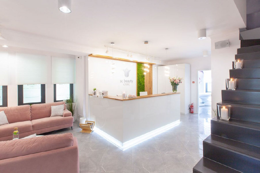 Jasne wnętrze kliniki z recepcją, różową sofą i schodami z dekoracyjnymi świecami.