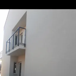 Jasna elewacja budynku z balkonem z czarną balustradą i białymi ramami okiennymi, widok z dołu.