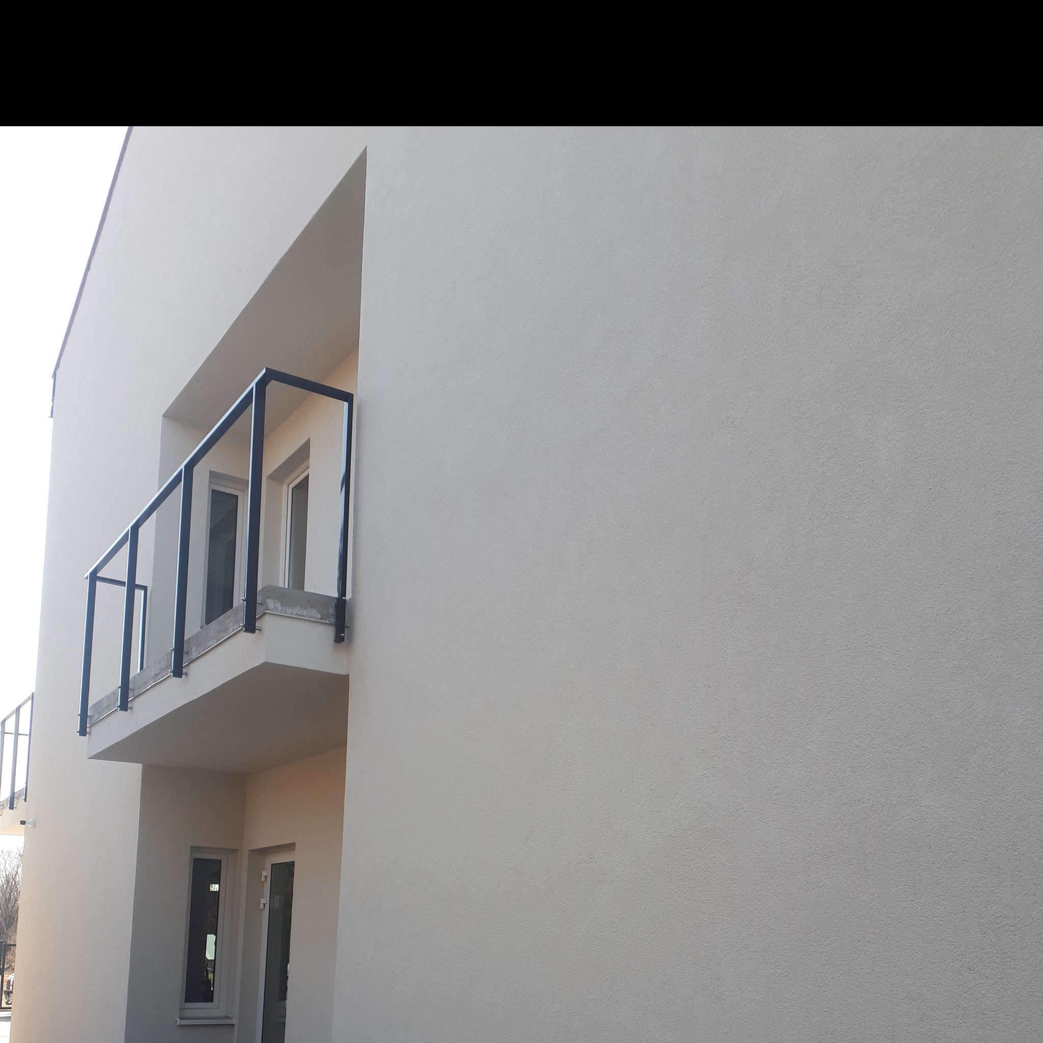 Jasna elewacja budynku z balkonem z czarną balustradą i białymi ramami okiennymi, widok z dołu.