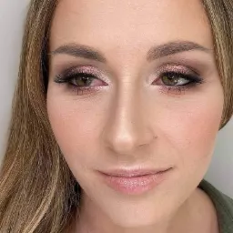 Portret kobiety z profesjonalnym makijażem, uwydatnione oczy z różowymi cieniami i sztucznymi rzęsami, delikatny róż na policzkach, brązowe włosy opadające na ramiona.