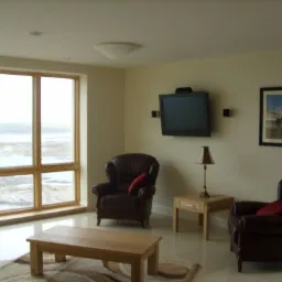 Jasne wnętrze salonu z dużym oknem z widokiem na morze, dwoma skórzanymi fotelami, drewnianym stolikiem kawowym na wzorzystym dywanie, lampą stołową i telewizorem na ścianie, całość w neutralnej...