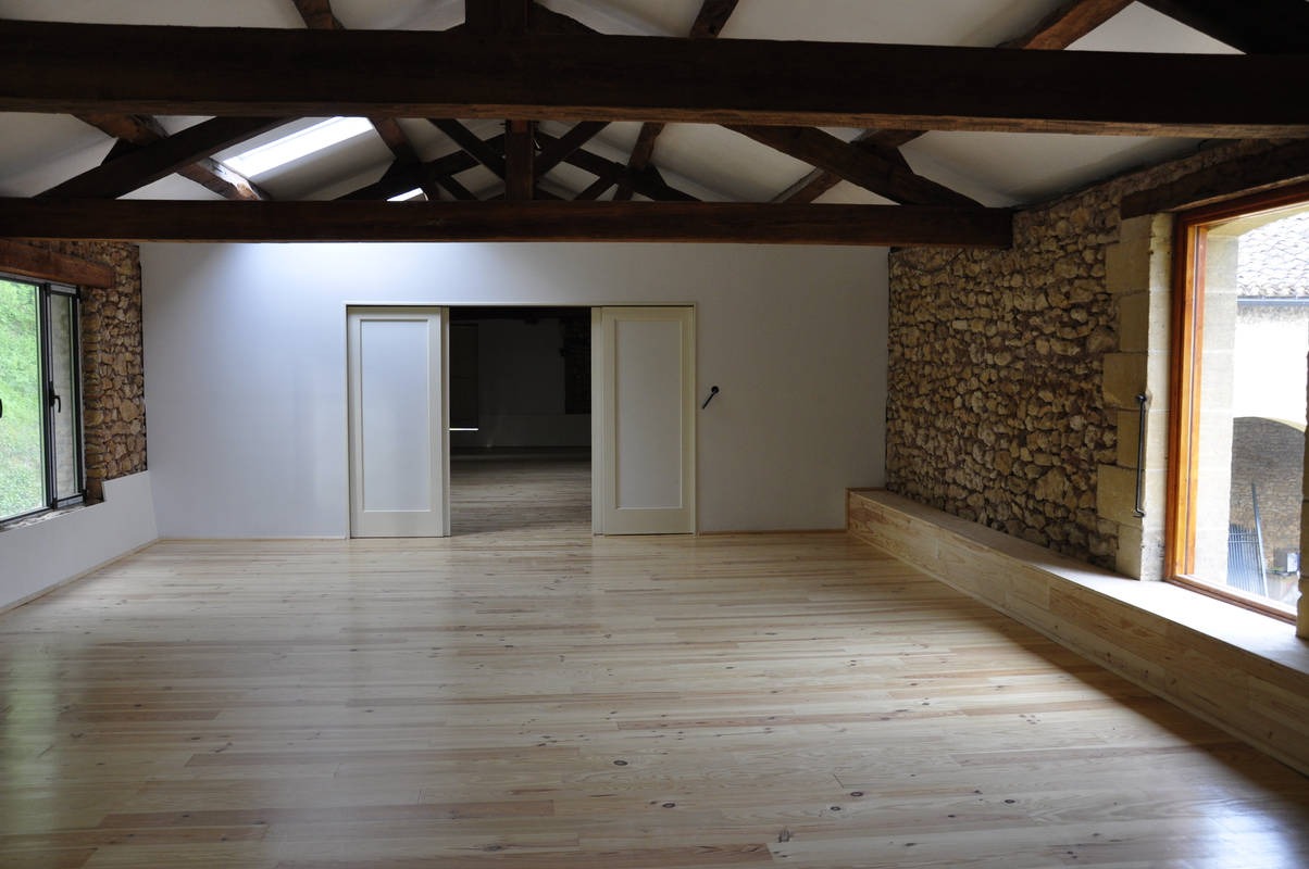 Wnętrze pokoju po remoncie w Brzesku: jasna drewniana podłoga, ściana z kamienia, białe ściany, drewniane belki stropowe i przesuwne drzwi.