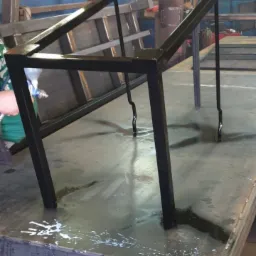 Malowanie natryskowe czarnej, metalowej konstrukcji stołu spawalniczego w warsztacie, z widocznymi śladami farby na stole roboczym.