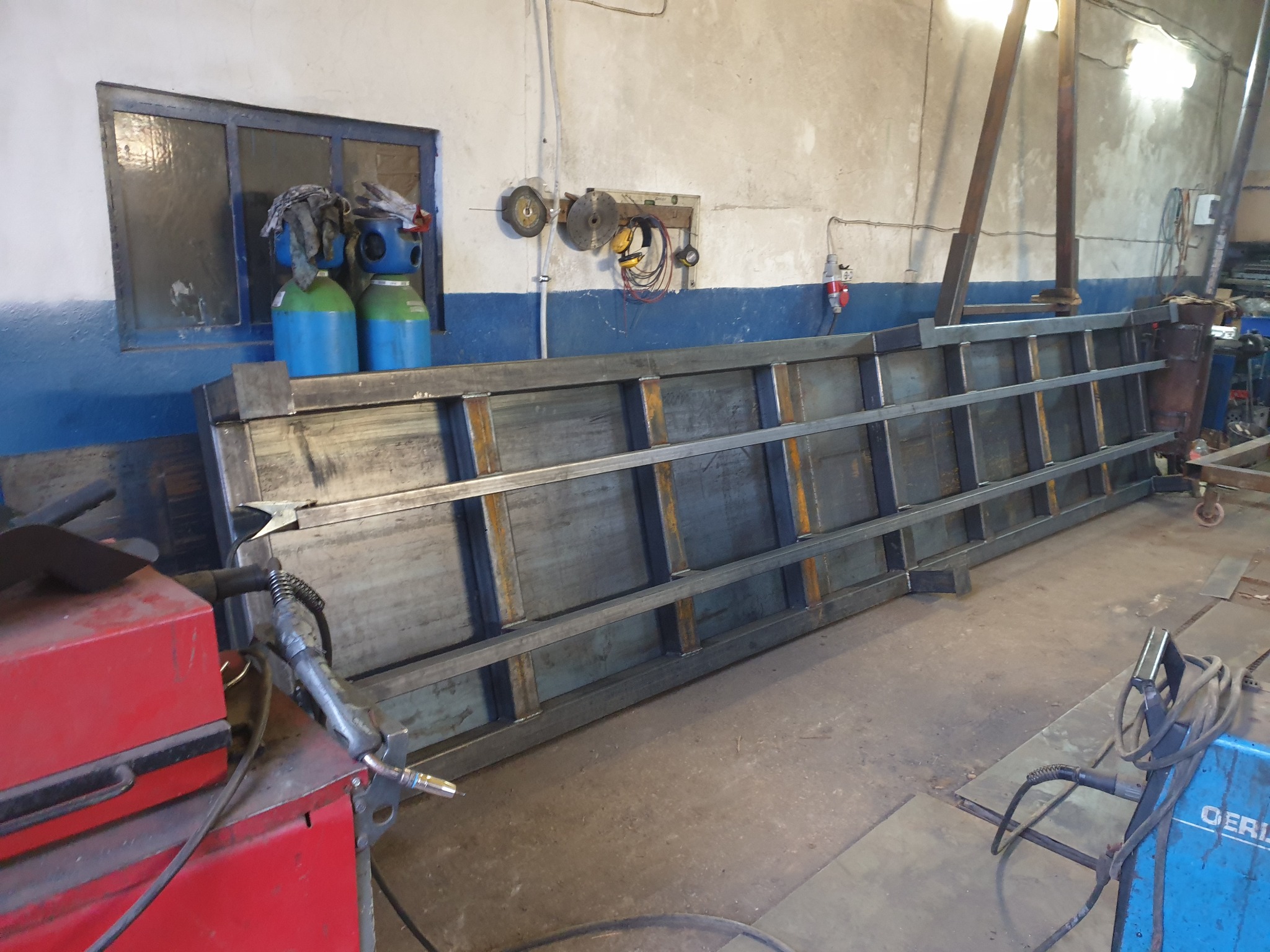 Stalowa konstrukcja ramy z profilami, spawana w warsztacie, widoczne butle z gazem i narzędzia spawalnicze