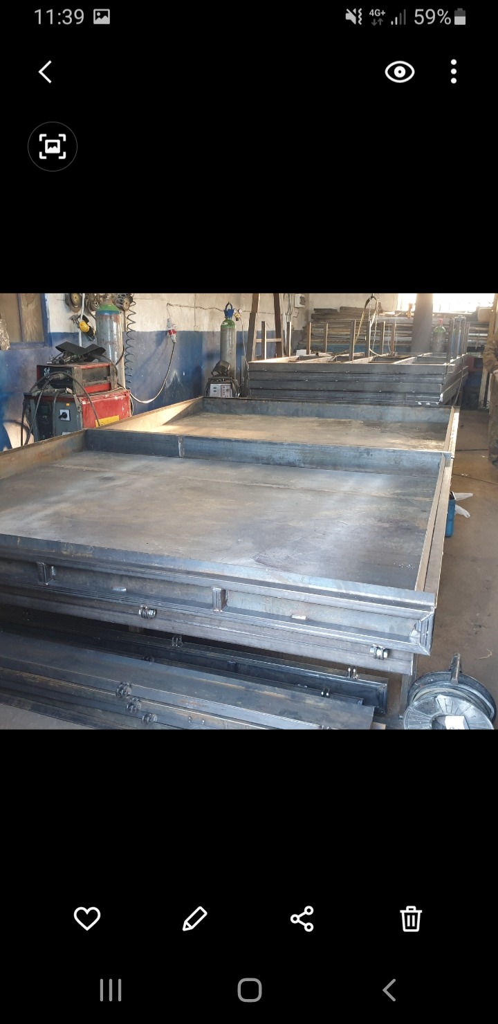 Stalowe ramy i belki ułożone w warsztacie, widoczne spawarki i butle z gazem, przygotowane do dalszej obróbki lub montażu.