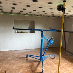 ITS PRO Tomasz Bar - Montaż płyt gipsowo-kartonowych na suficie z użyciem podnośnika i lasera poziomującego, widoczne profile i elementy mocujące.