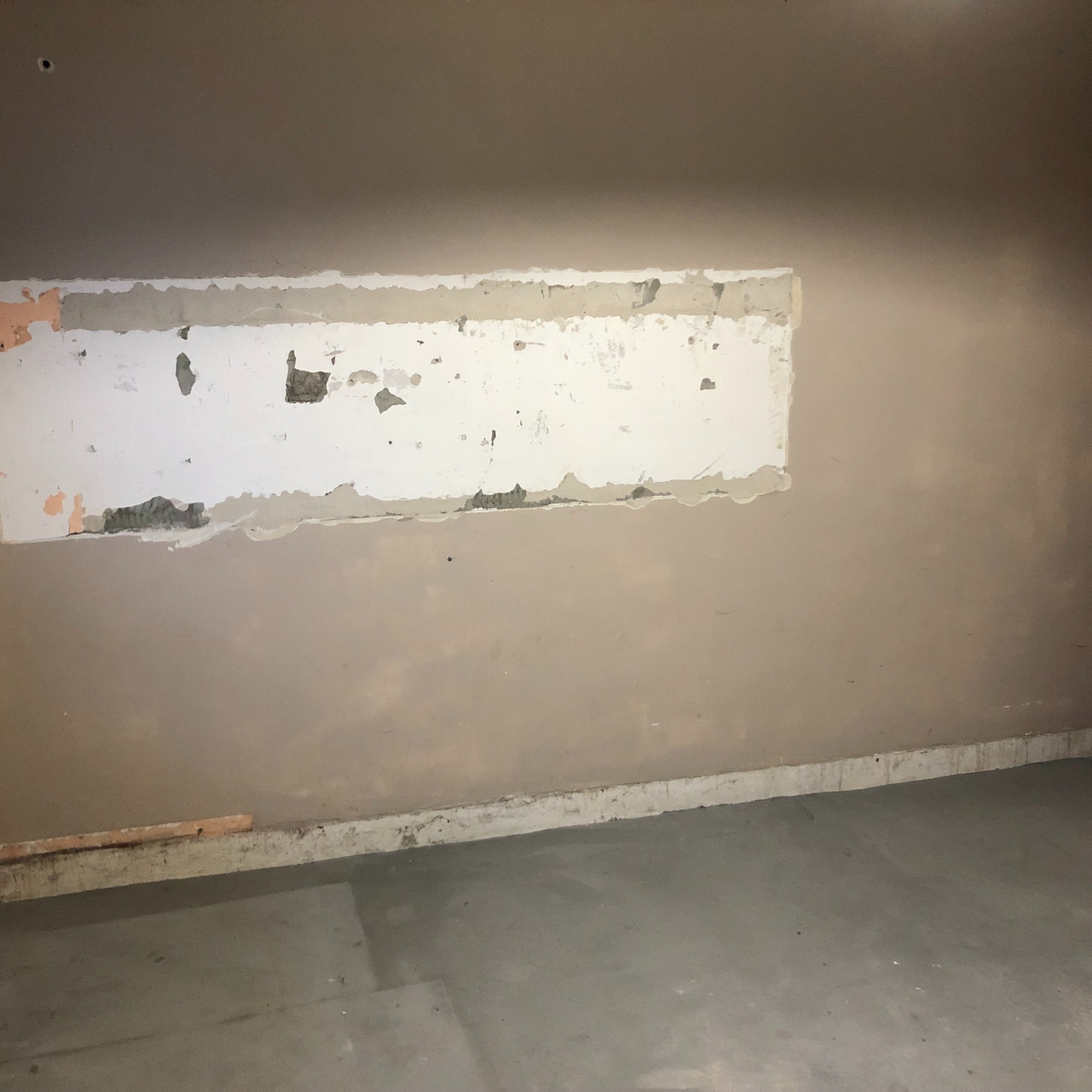 Przygotowanie ściany do malowania: fragment ściany z usuniętą starą powłoką, widoczne warstwy tynku i farby, surowy betonowy podkład.