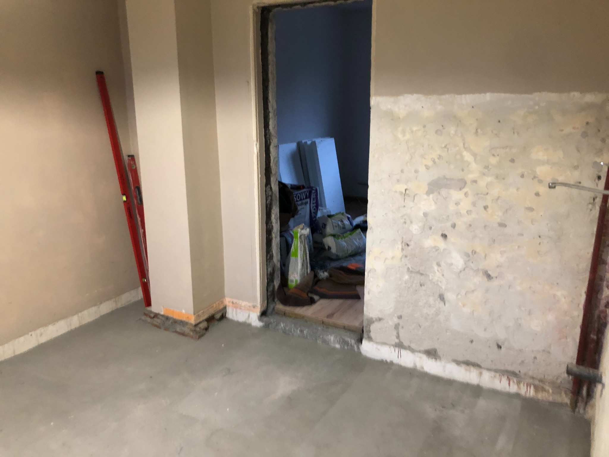 Stan surowy mieszkania w Kraśniku: ściany przygotowane do prac wykończeniowych, widoczne worki z materiałami budowlanymi i poziomica oparta o ścianę.