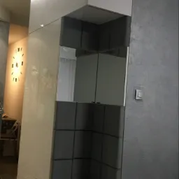 Wnęka z siedziskiem obita szarą tapicerką, wkomponowana w białą szafę z połyskiem, oświetlenie LED w górnej części szafy, widoczny fragment zegara na ścianie w tle.