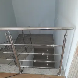 Polerowana metalowa barierka schodowa z kulistymi elementami dekoracyjnymi, widok z góry na schody z jasnego kamienia.