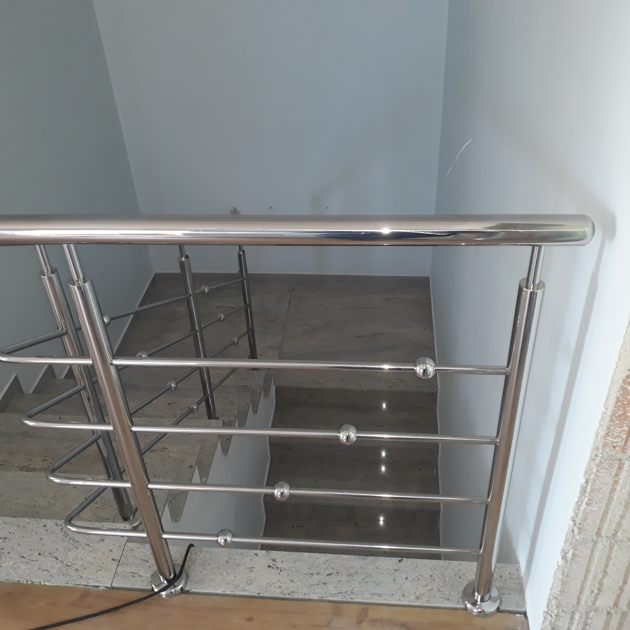 Polerowana metalowa barierka schodowa z kulistymi elementami dekoracyjnymi, widok z góry na schody z jasnego kamienia.