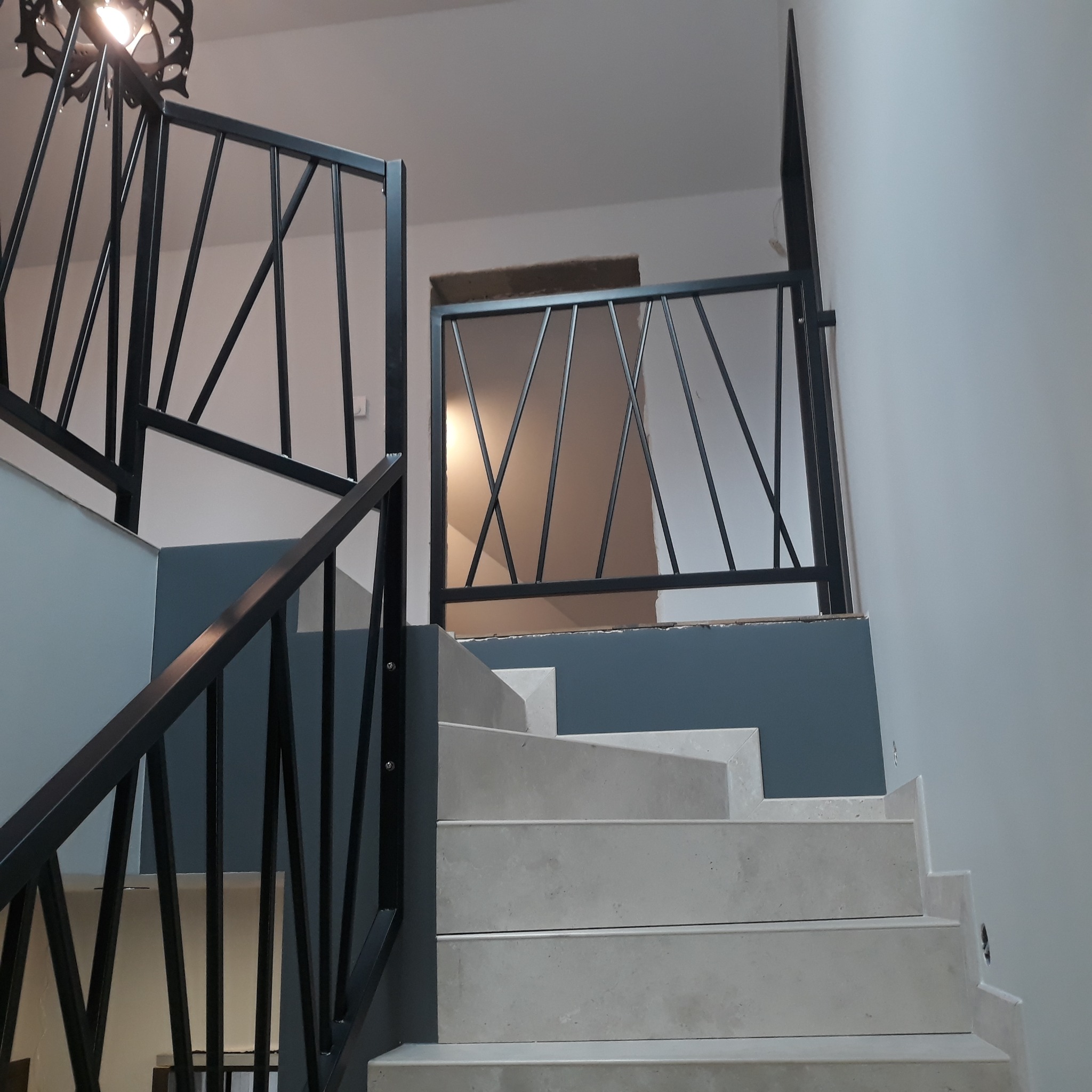 Schody z jasnego kamienia z czarną metalową konstrukcją zabezpieczającą, widok z dołu.