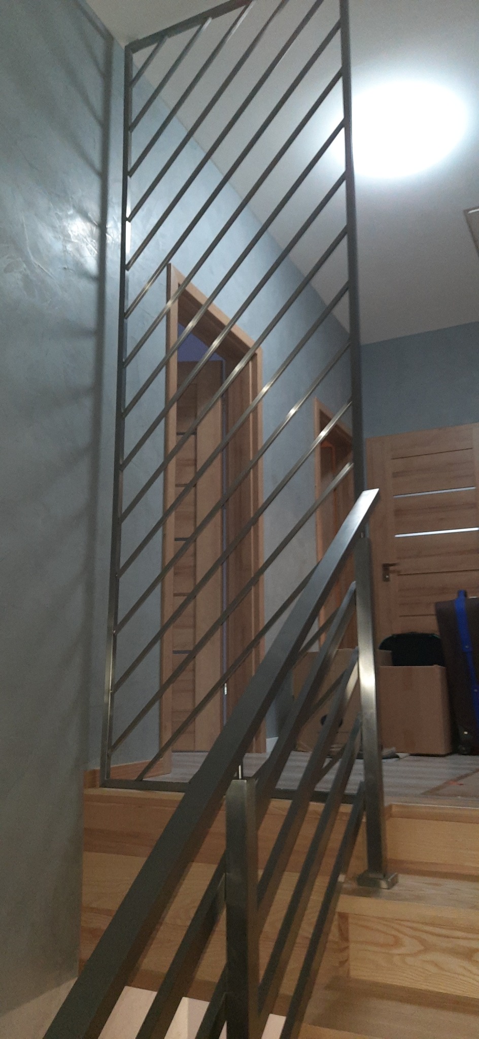 Metalowa konstrukcja z ukośnymi prętami na schodach, widoczne drzwi w tle.