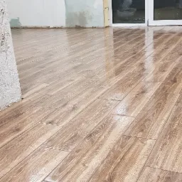 Świeżo ułożone, błyszczące panele podłogowe imitujące drewno, ułożone skośnie w pokoju w trakcie remontu, z widocznymi niedokończonymi ścianami i listwami przypodłogowymi.