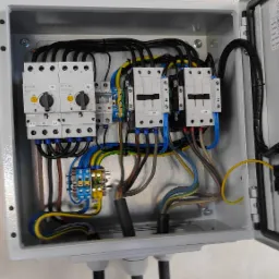 Otwarta rozdzielnica elektryczna z zamontowanymi stycznikami, wyłącznikami silnikowymi Eaton oraz listwami zaciskowymi, z widocznymi przewodami w różnych kolorach, zainstalowana na ścianie.