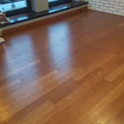 Ułożona podłoga bambusowa z widocznym opakowaniem paneli, biała ściana z cegieł w tle, okno z ciemną ramą.