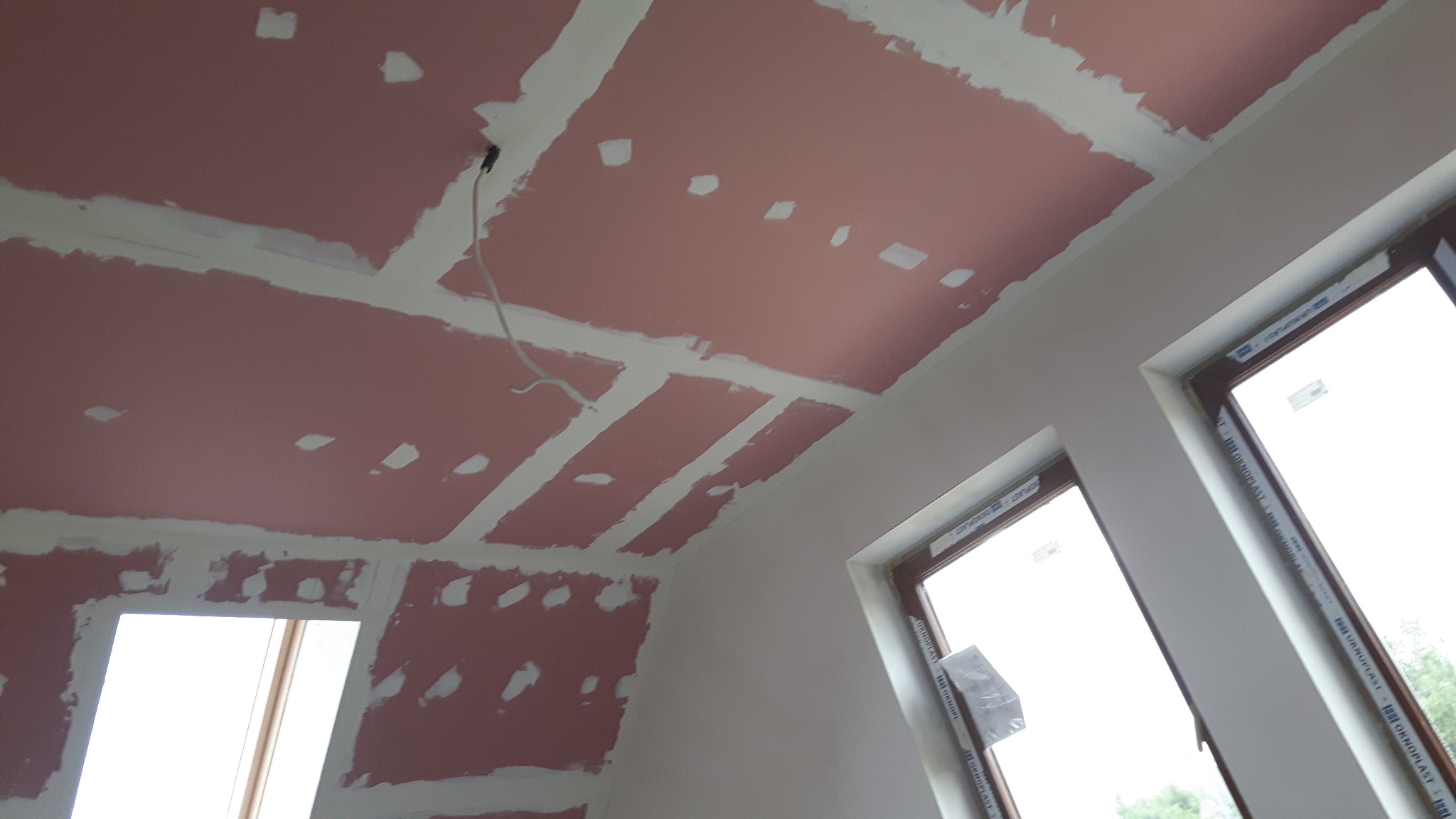 Montaż płyt gipsowo-kartonowych na suficie poddasza, widoczne łączenia zbrojone taśmą, przygotowanie do szpachlowania, dwa okna dachowe w tle.