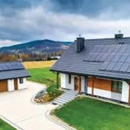 Dom jednorodzinny z zainstalowanymi panelami słonecznymi na dachu domu i garażu, widoczne logo firmy Columbus Energy w lewym dolnym rogu.