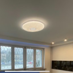 ROYAL BUD Kompleksowe Wykończenia wnętrz YURII TYMOSHCHUK - Wnętrze po remoncie w Warszawie: gładkie, białe ściany, okna z ozdobnymi szprosami, nowoczesna lampa sufitowa i podświetlenie LED wzdłuż okna.