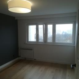 ROYAL BUD Kompleksowe Wykończenia wnętrz YURII TYMOSHCHUK - Jasny parkiet w pustym pokoju po remoncie, z szarą ścianą akcentującą, białymi oknami i nowoczesną lampą sufitową.