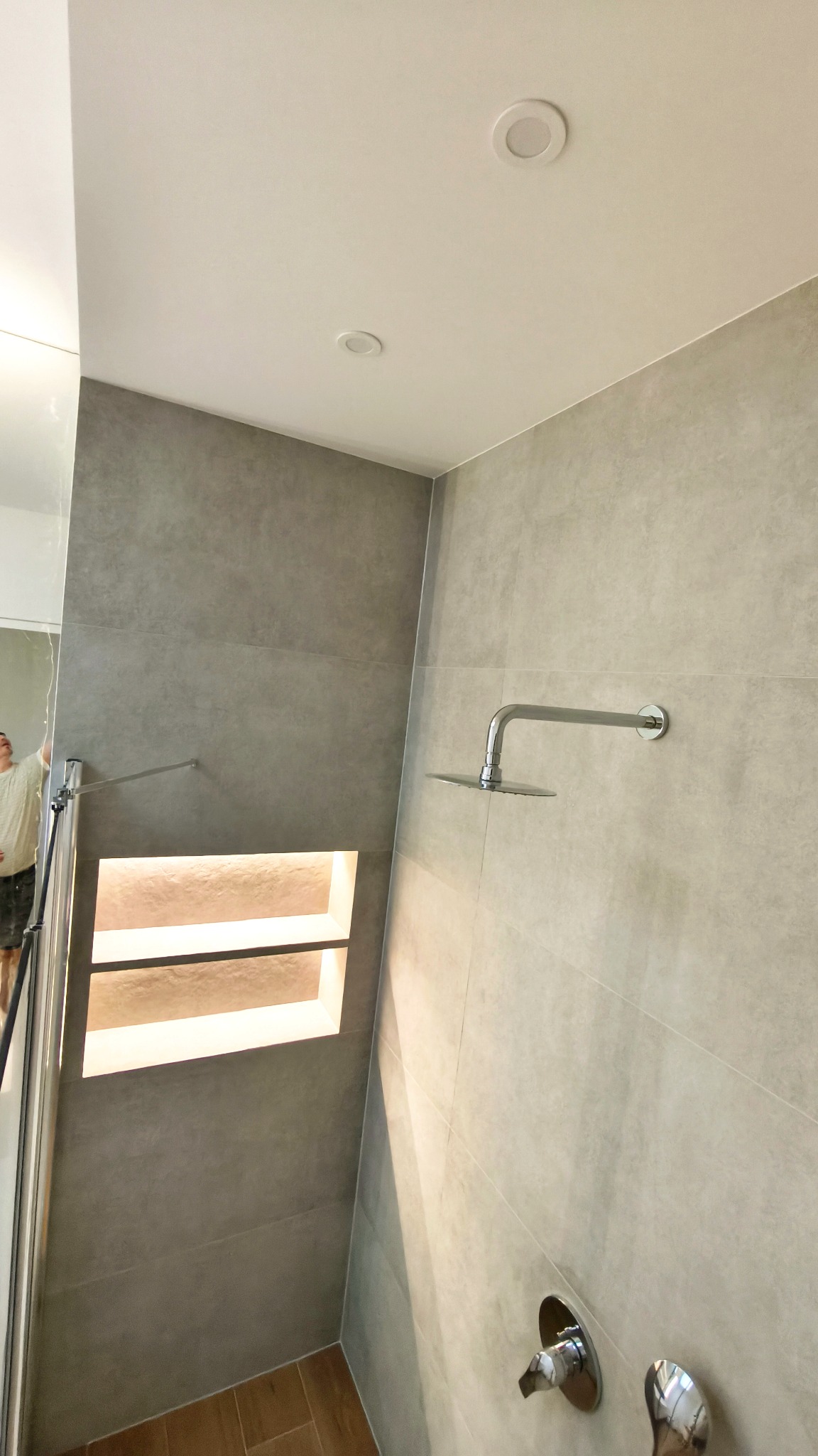 Nowoczesna kabina prysznicowa z szarymi płytkami, wnęką z podświetleniem i deszczownicą. Minimalistyczny design, widok z dołu.